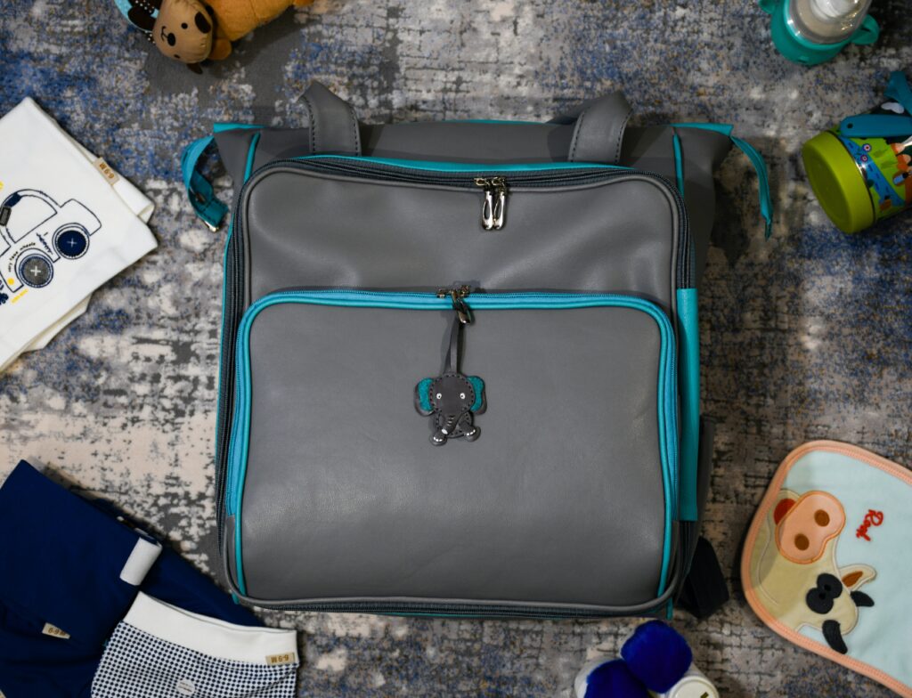 A grey and teal diaper bag surrounded by baby essentials.