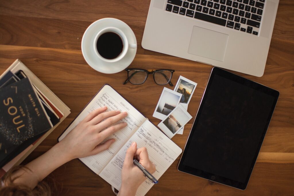 Woman writing in journal with cup of coffee and laptop on desk