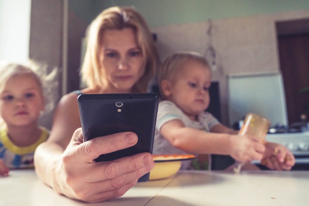 A woman uses smartphone while sitting with children